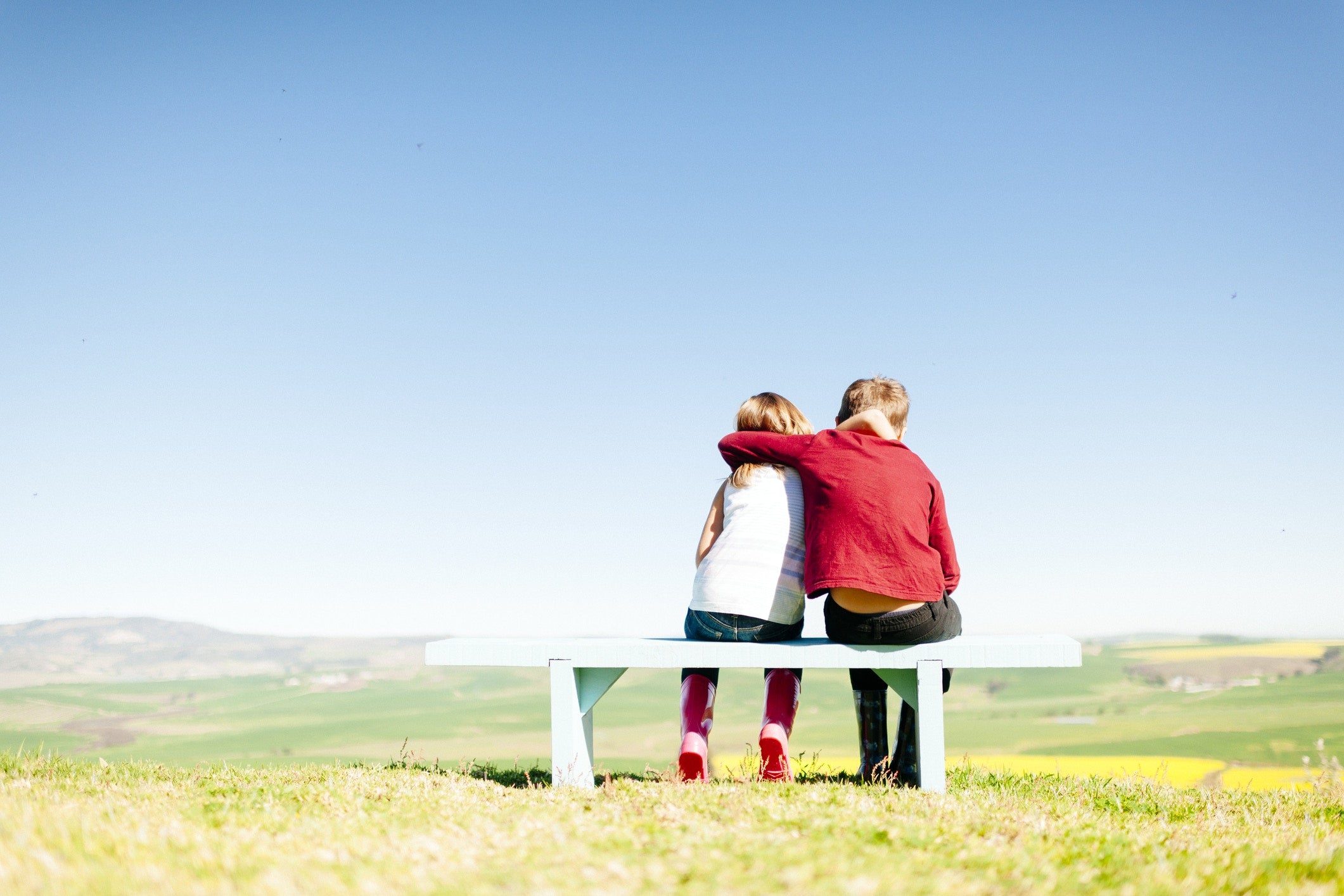 rear view of boy and girl sitting on bench at field