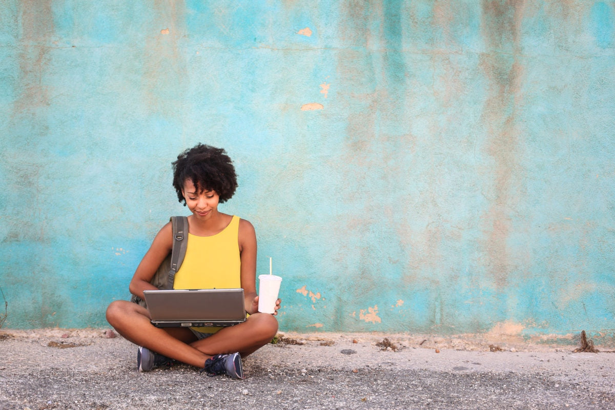A woman sitting on the road and using laptop