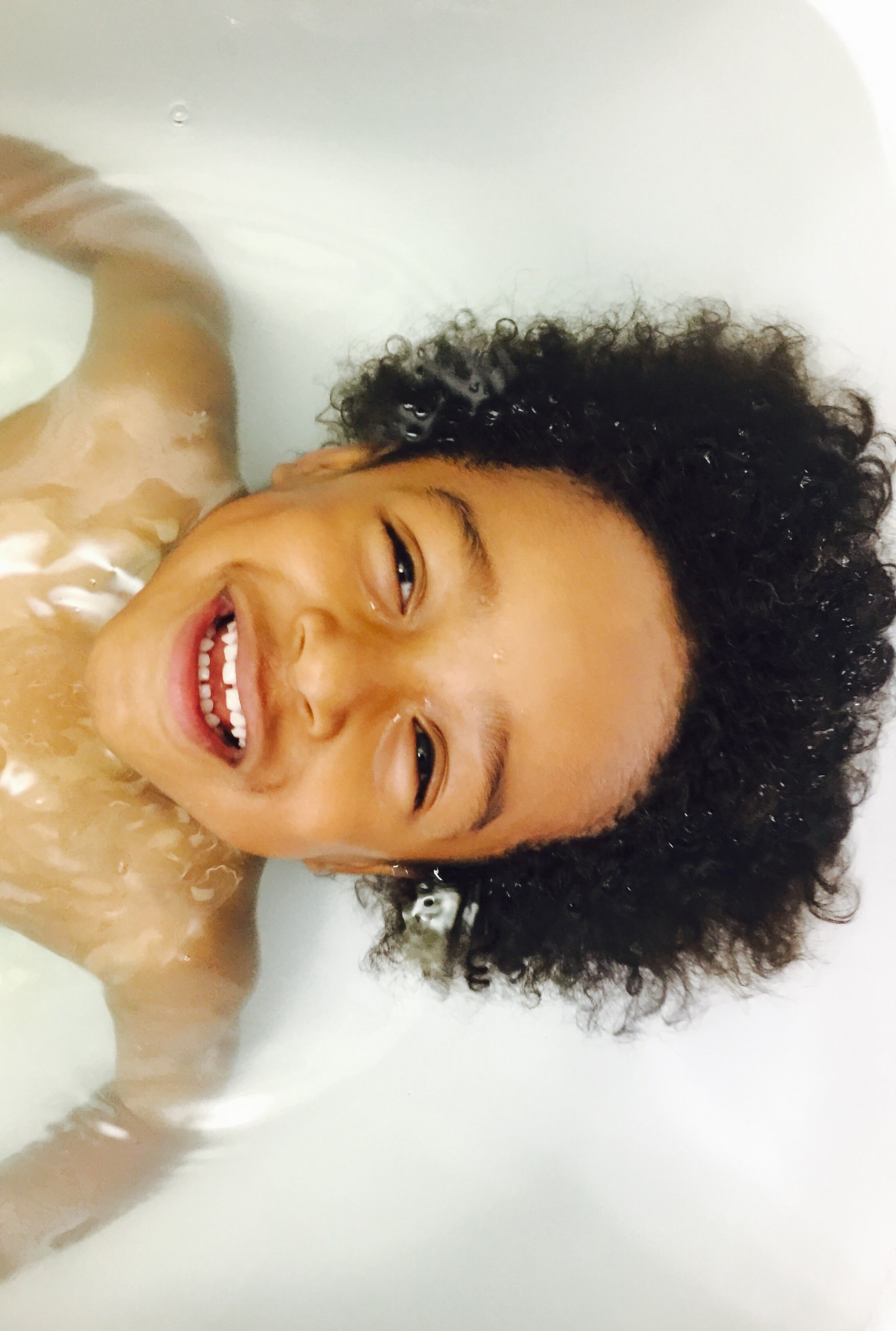 Little Boy with curly hair floating in Bathtub