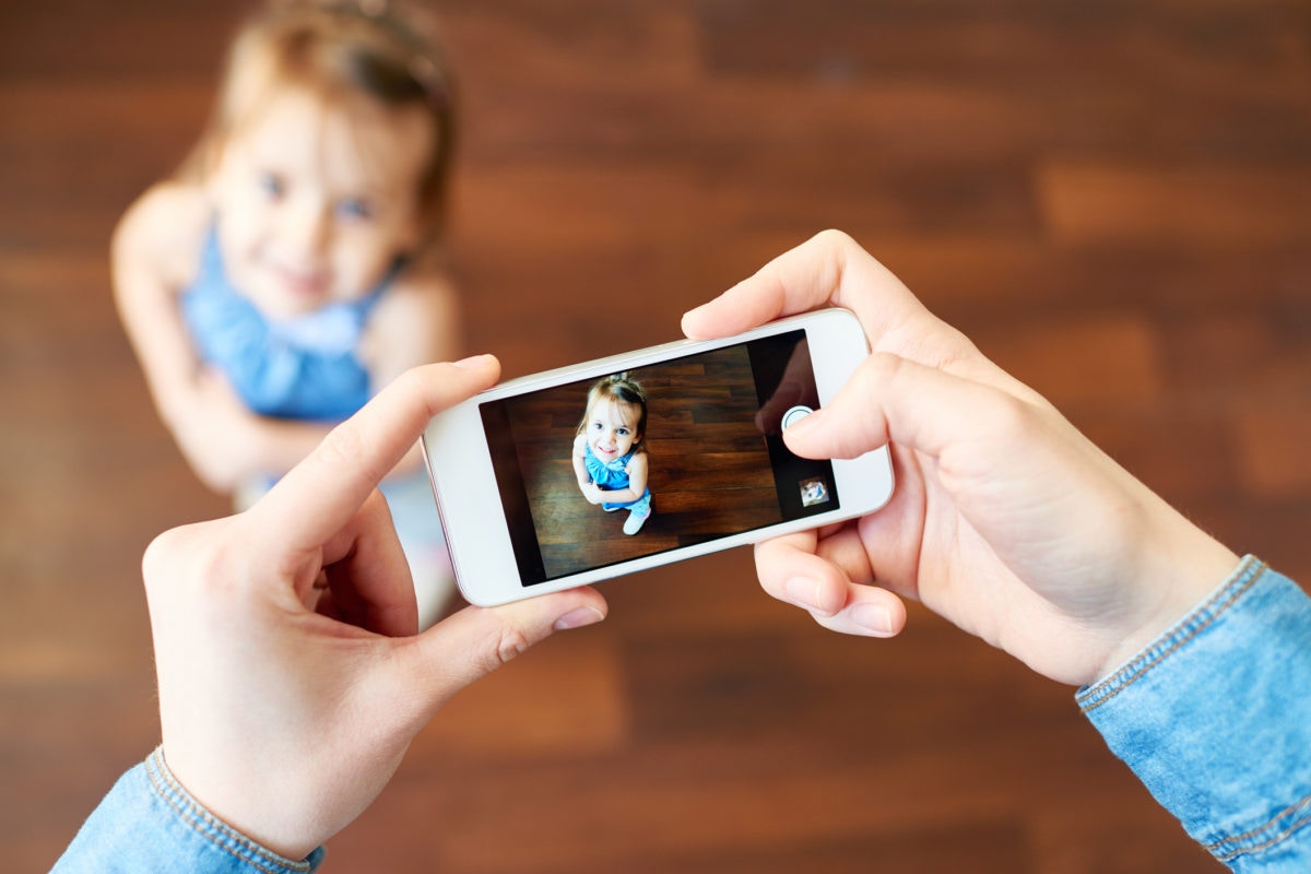 Parent holding phone taking photo of daughter on smartphone