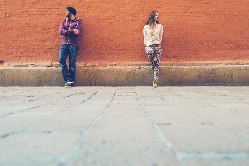 man and women standing in front of a brick wall few feet apart not looking at each other