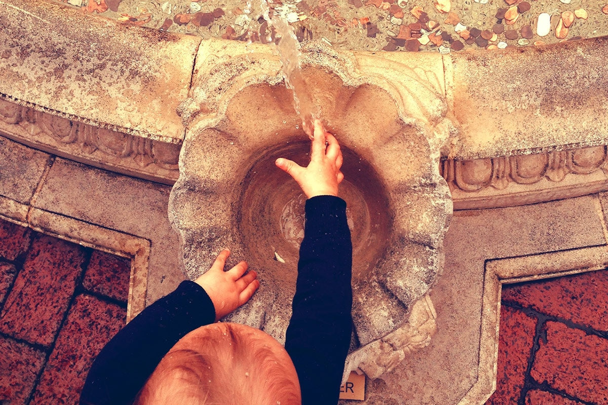 baby boy putting his hand in a small water fountain