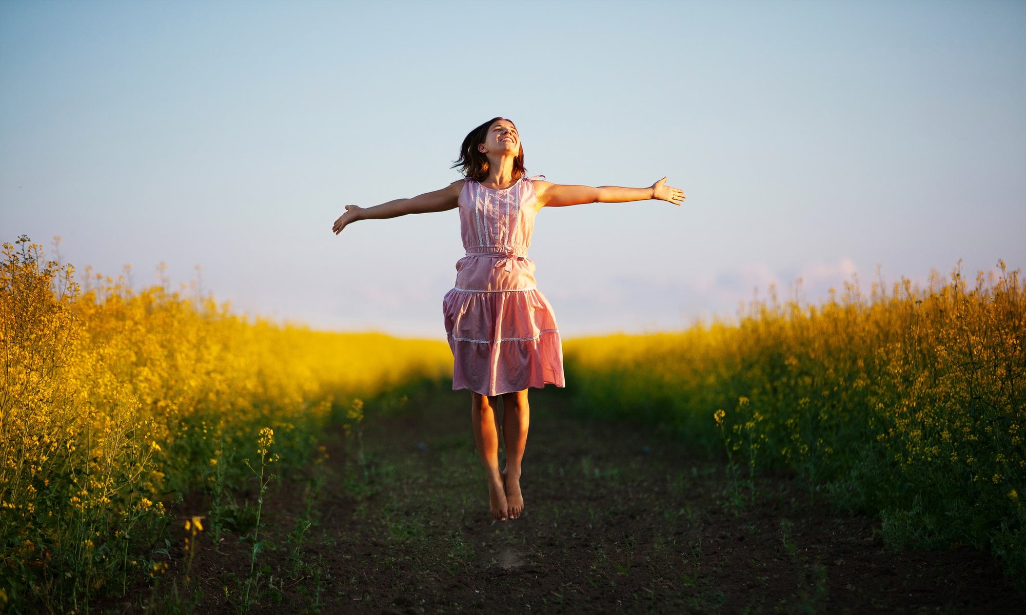 Young  woman jumping in the middle of a field with yellow flowers