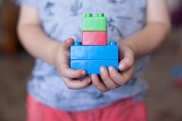  young boy playing with his building blocks holding a finished creation in his hands