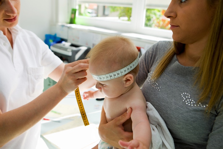 nurse measuring baby's head as child is being held by mother