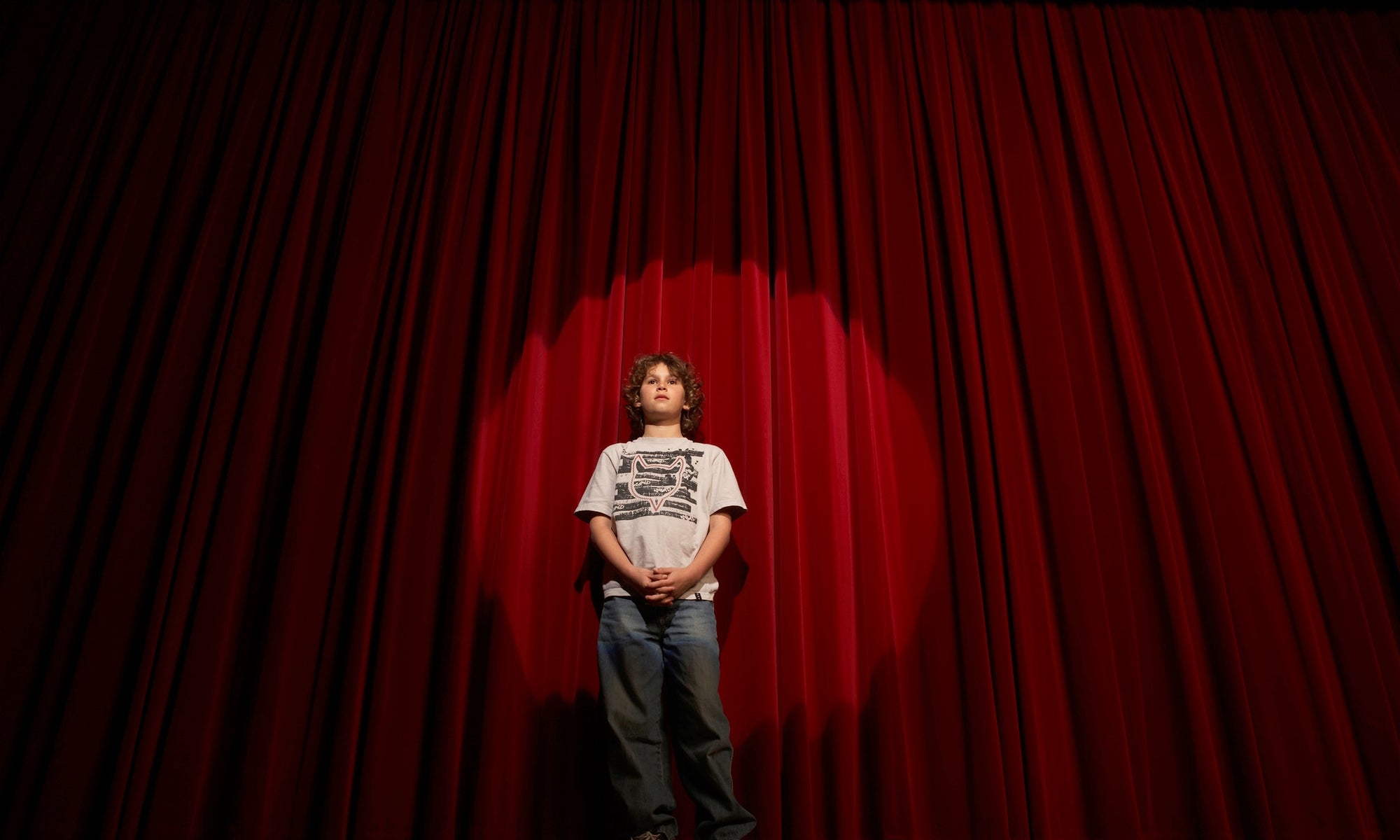  young boy performing at the stage with red curtains