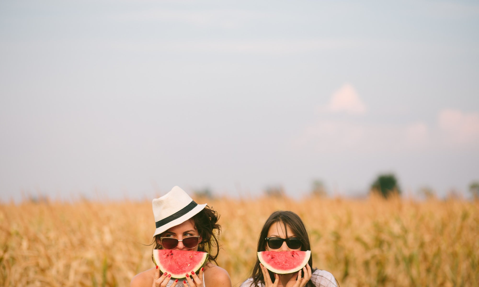 two beautiful womens covering face with watermelon in wheat field