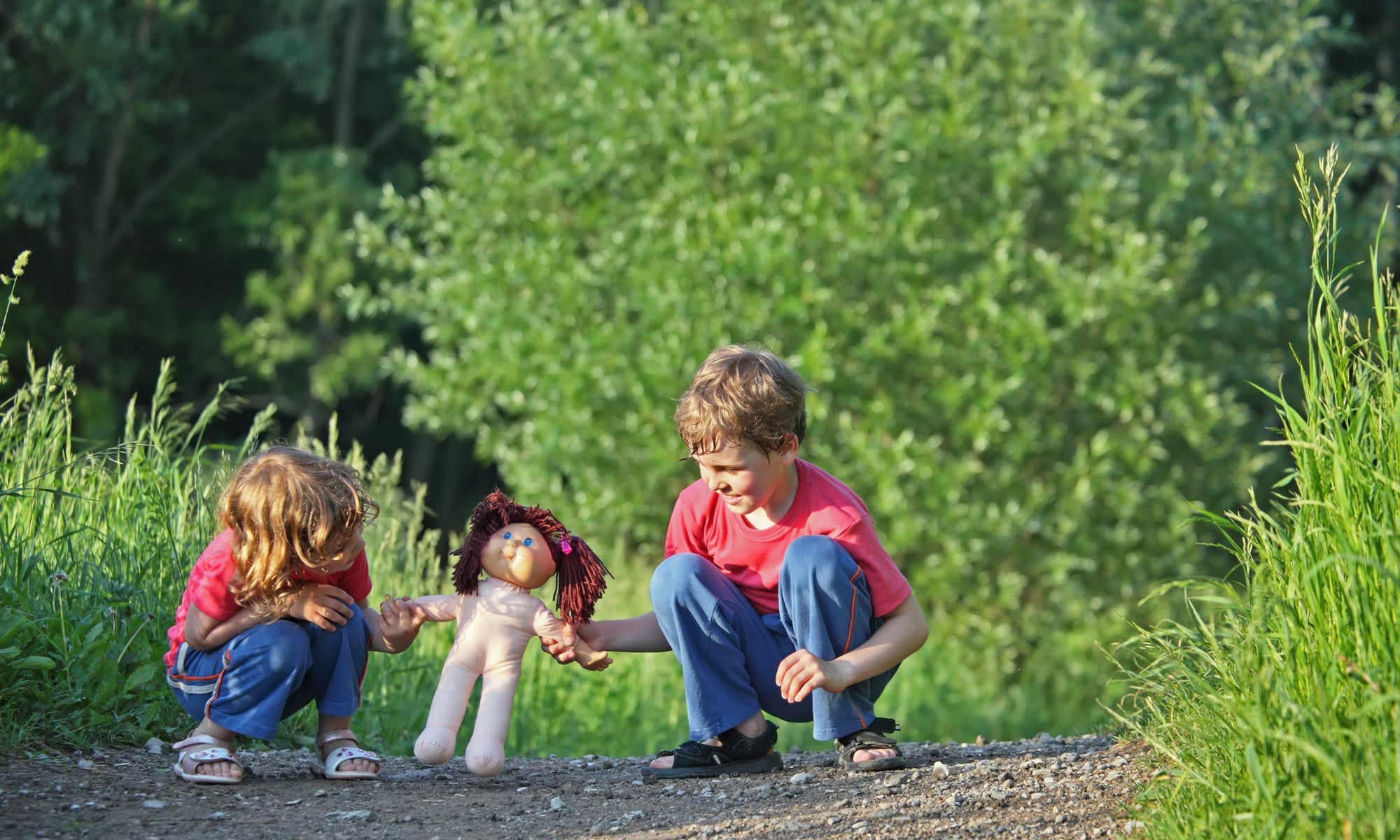 Little children boy and girl sitting on forest ground playing with doll