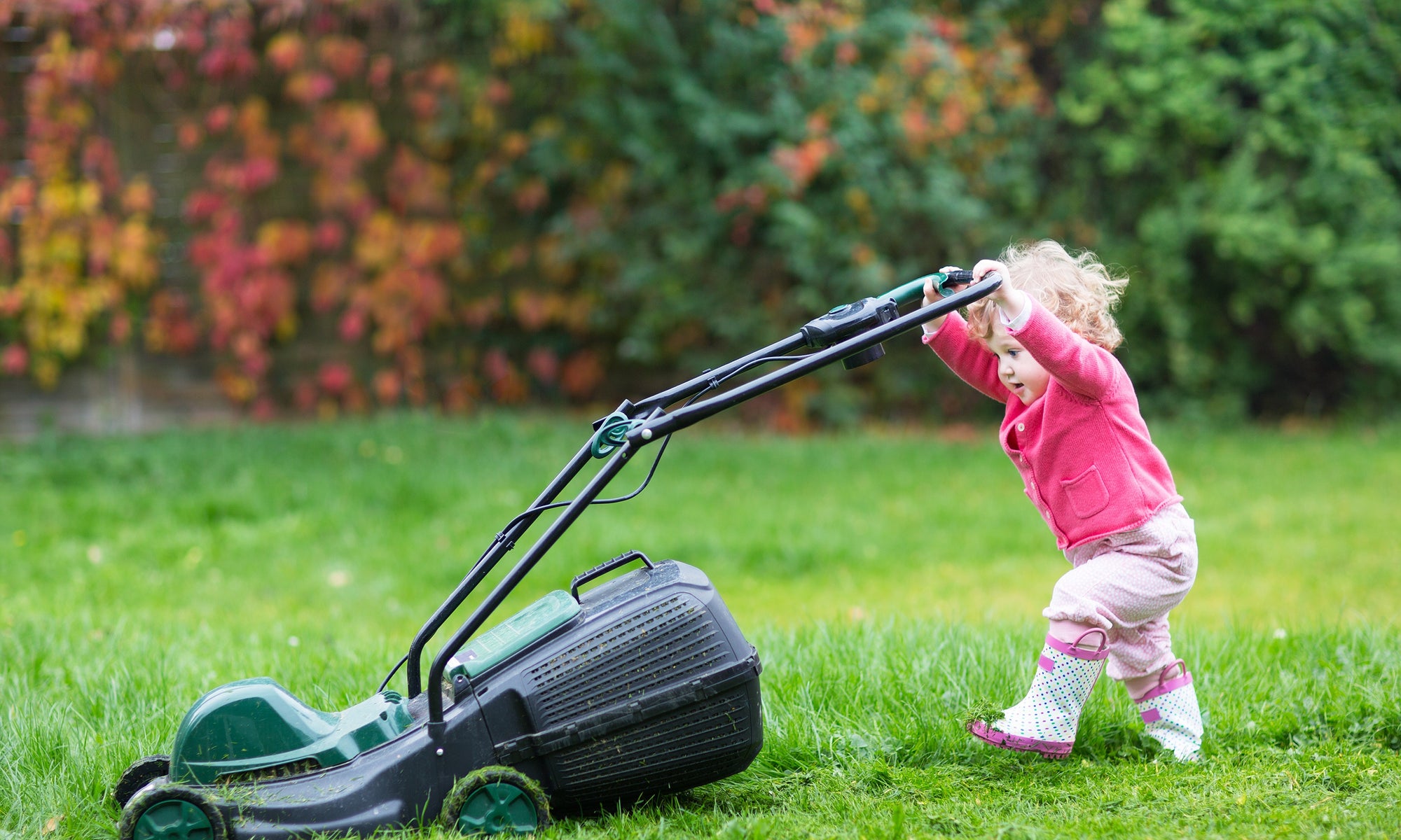 Cute curly baby girl  with big green lawn mower