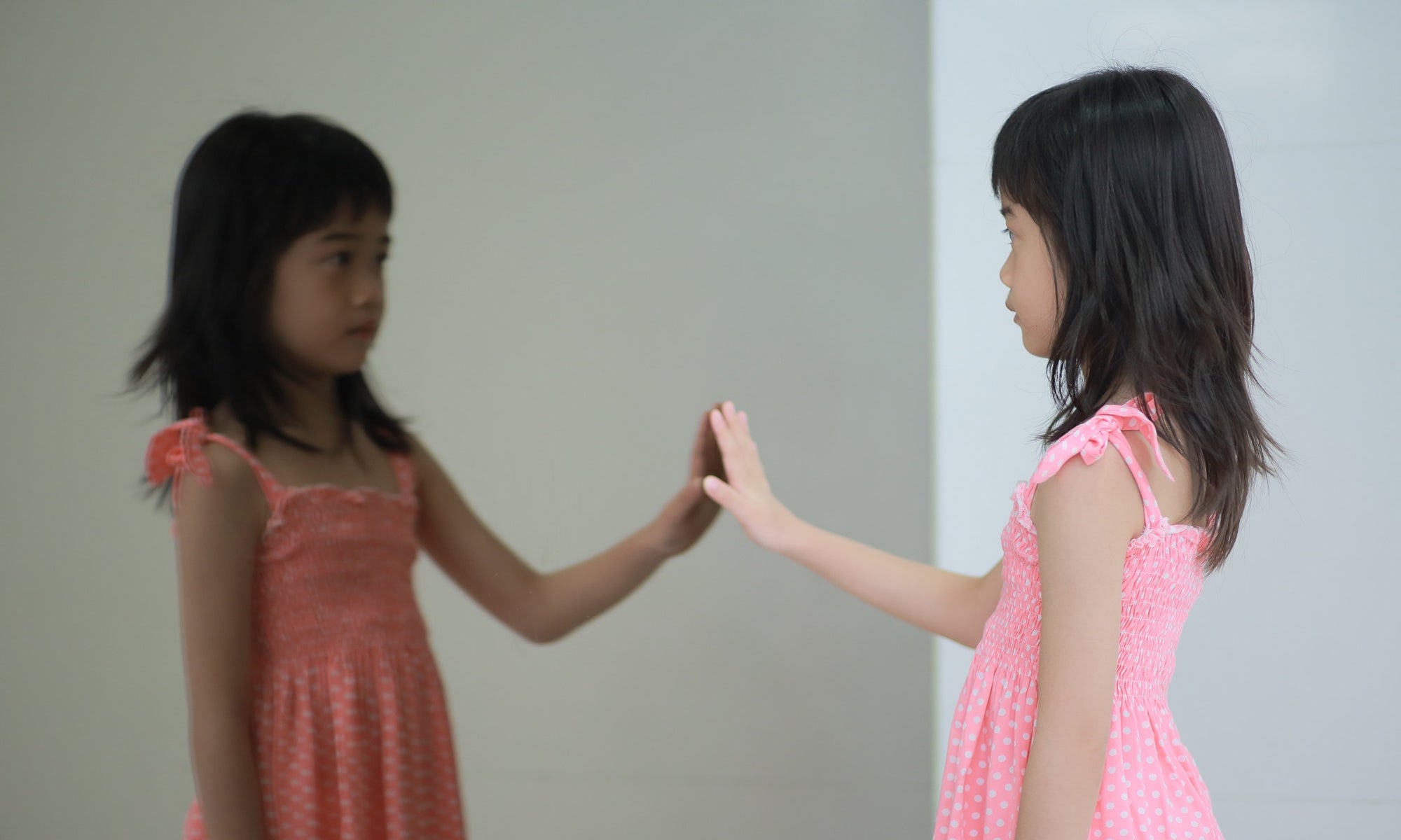 a girl touching the mirror and lookingat her reflection