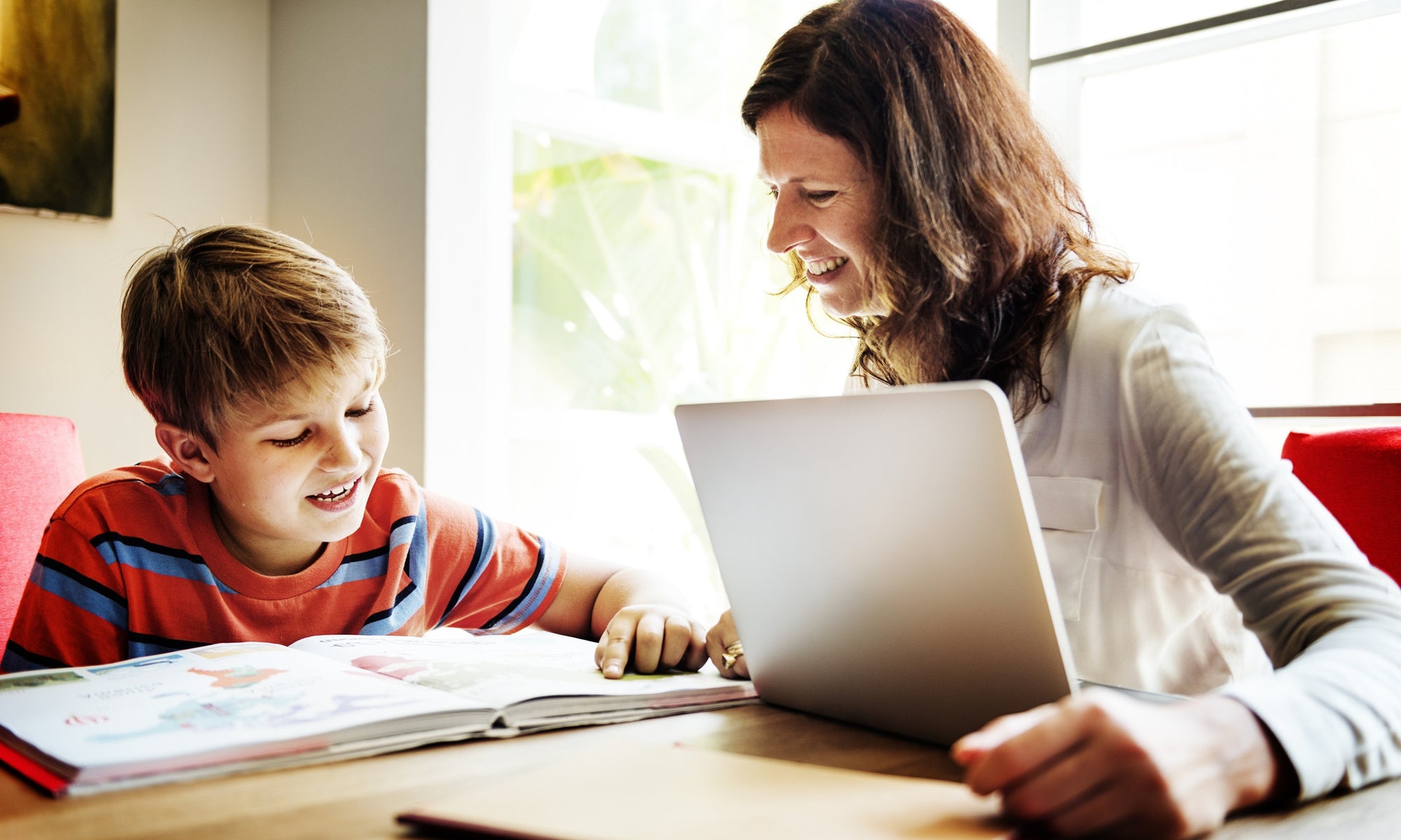 Mother helping son while he is studying and she is working on laptop at home 