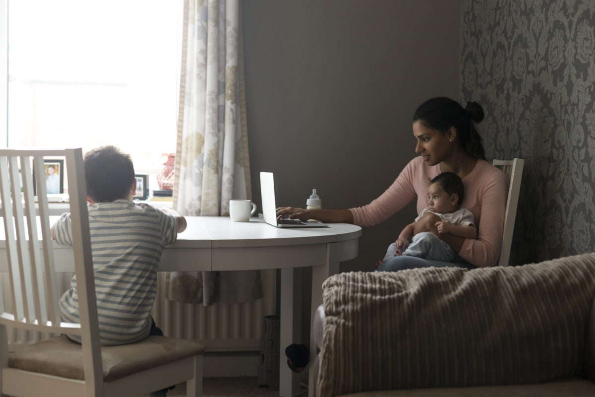 mother holding her baby boy on hands while working with laptop computer at home , elder son using phone