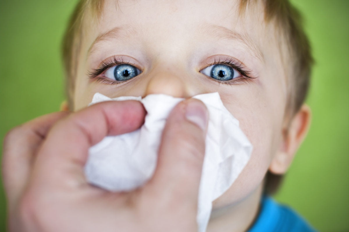 boy with blue eyes blowing nose to tissue