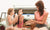 mother with two girls sitting in car trunk and having breakfast