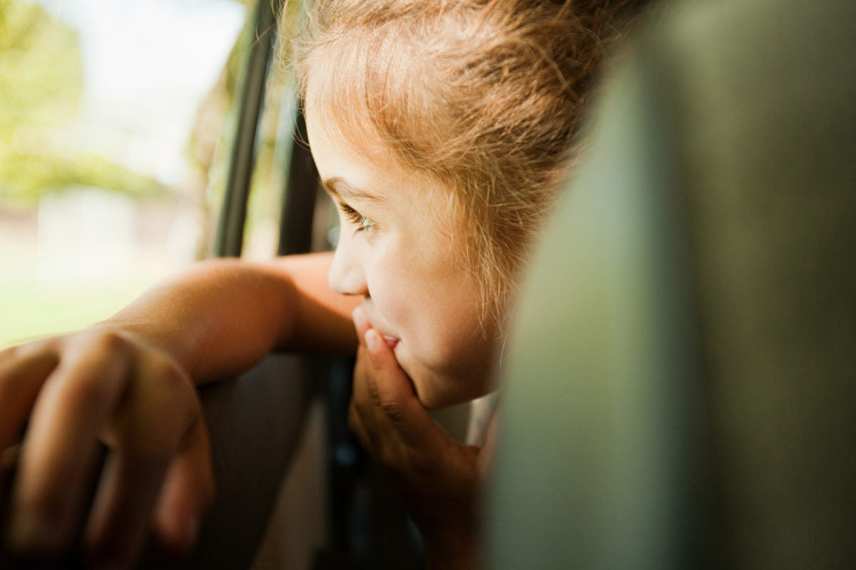 Little girl in car, looking out of window, smiling bt covering her mouth