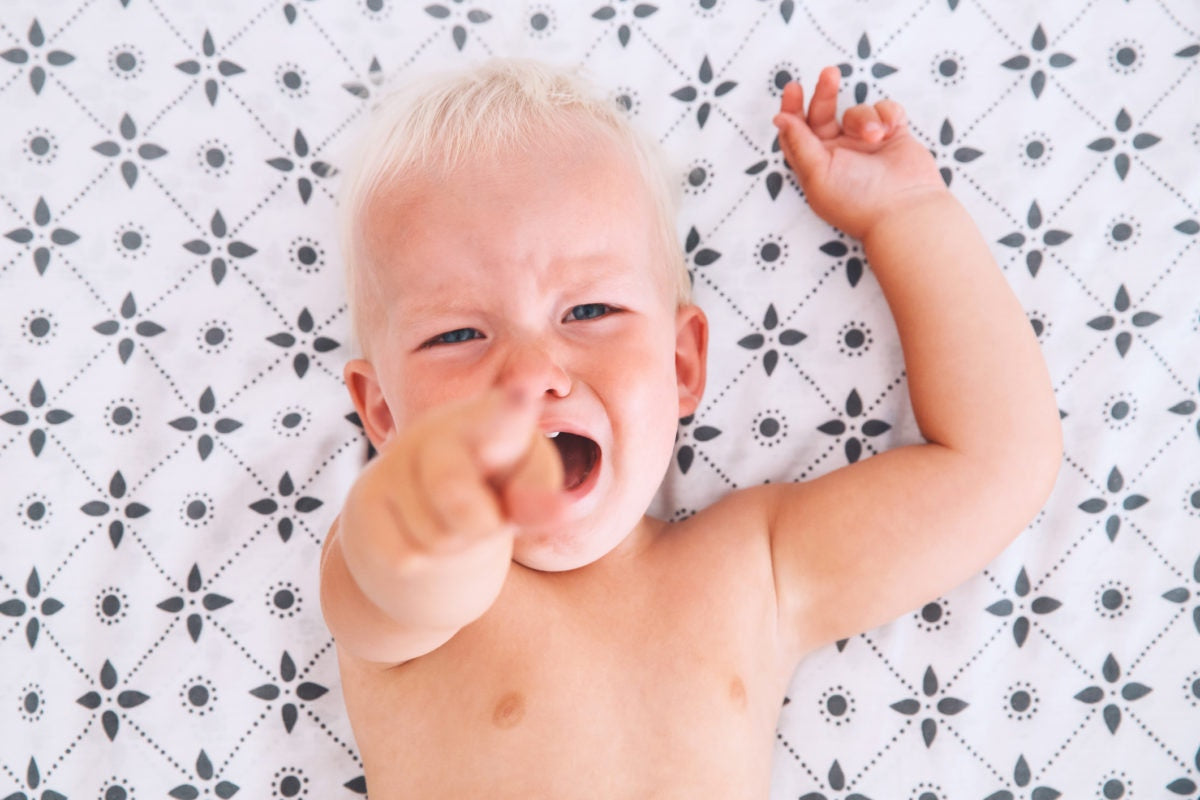 child lying in the bed, crying and points his finger at the camera