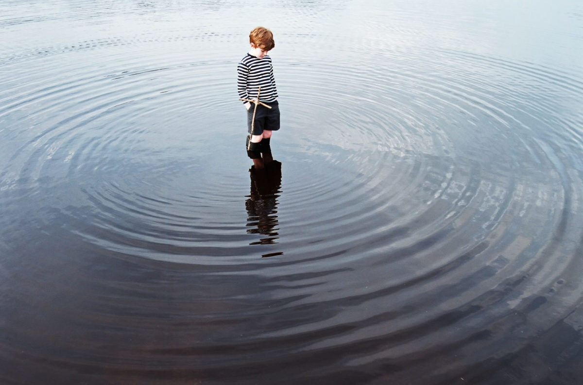 boy standing in a lake surrounded by ripples