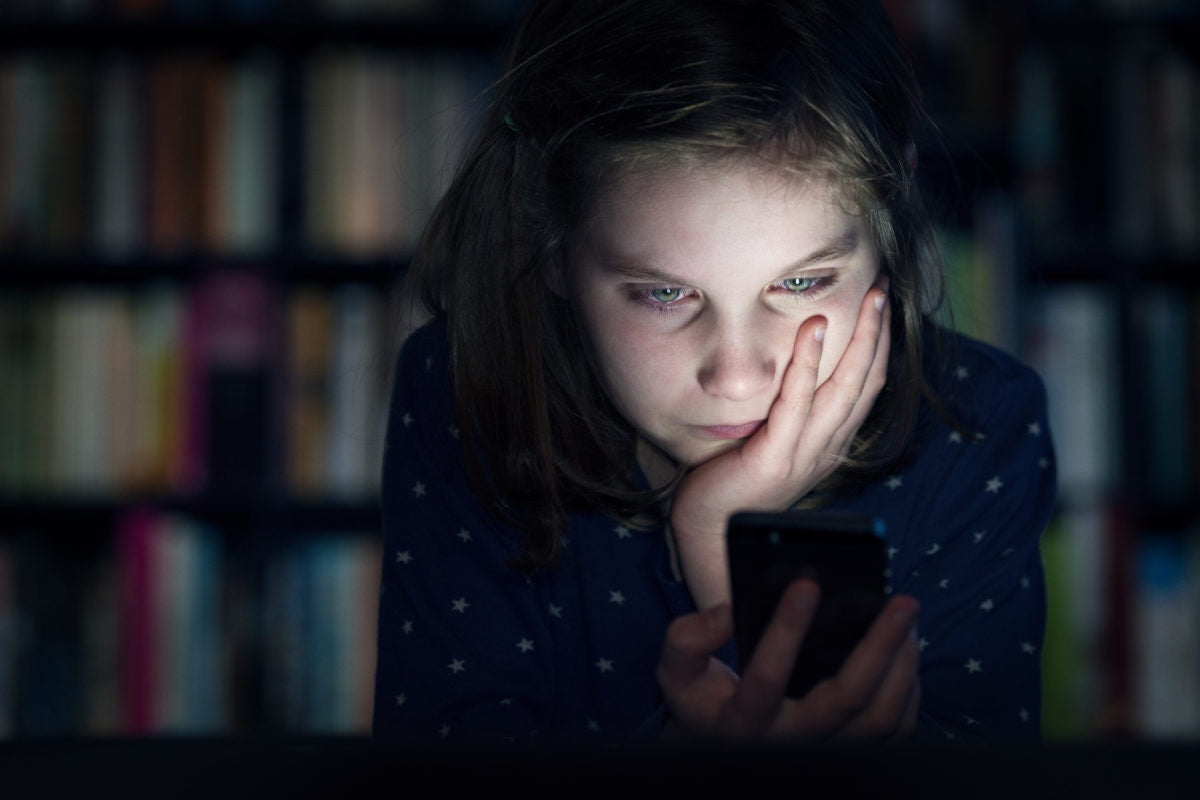 Young child girl using mobile phone in dark room, The light from the mobile reflect on her face