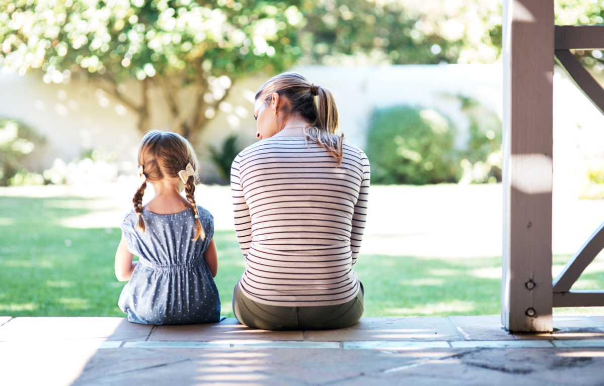 back view of young mother and daughter sitting on bench in veranda