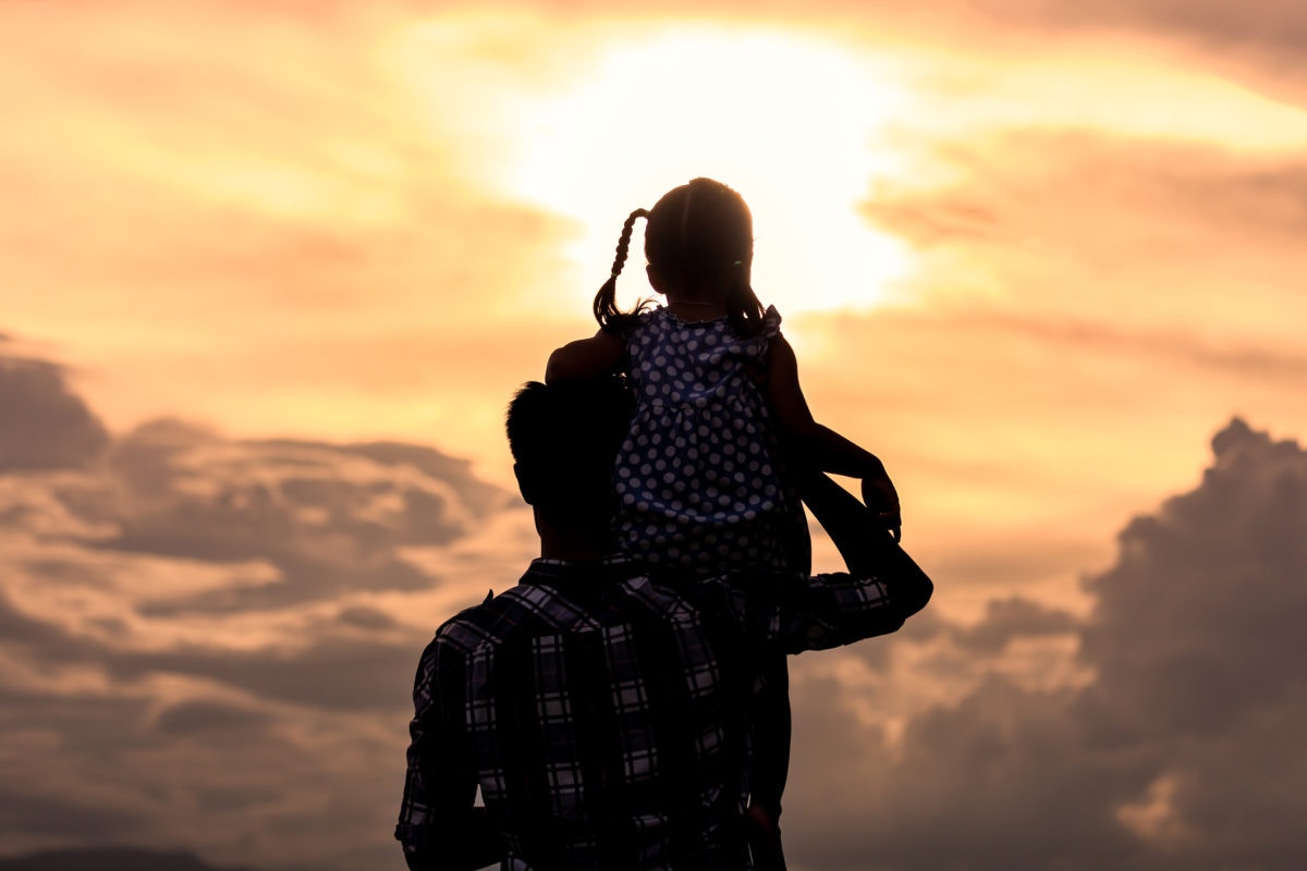 Baby sitting on shoulder of father and looking at sun set