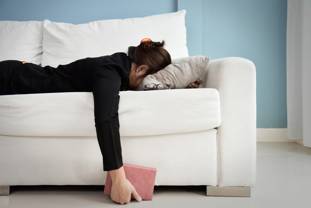 Woman lying in couch with face buried in pillow  and a book in her hand