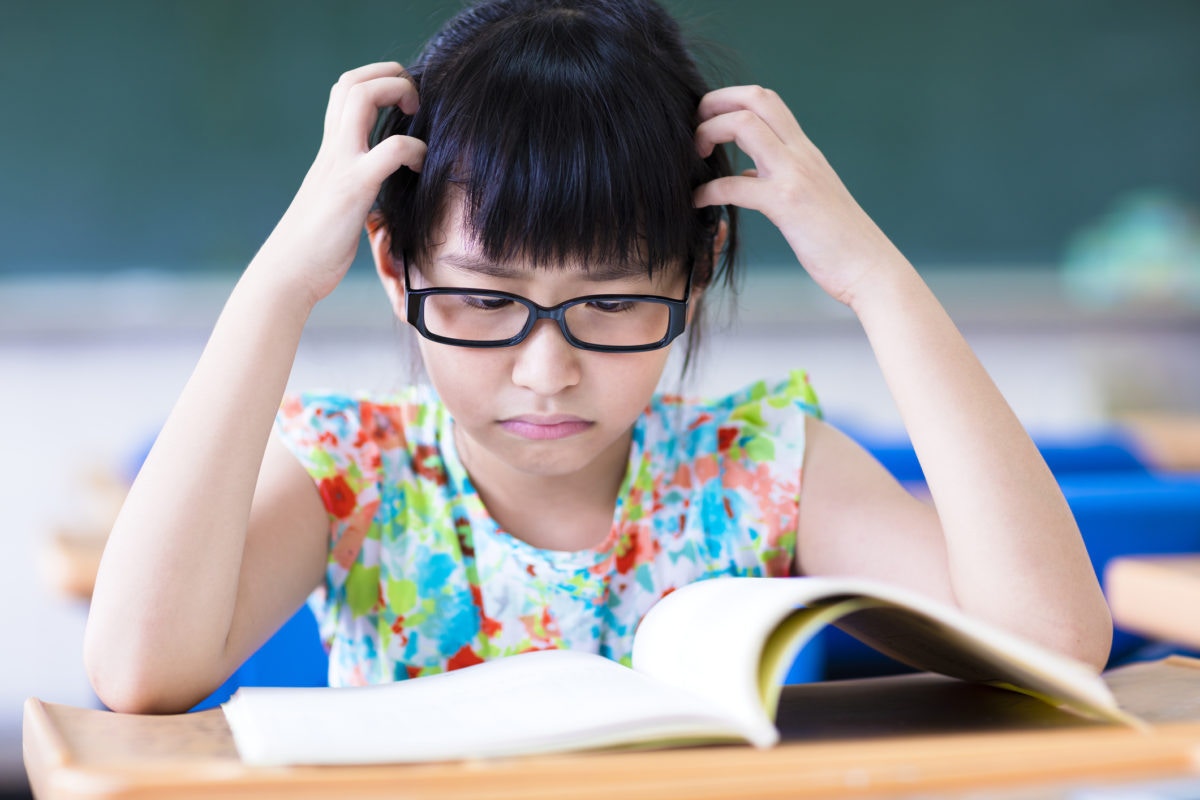 A chinese girl reading book by scartching her head