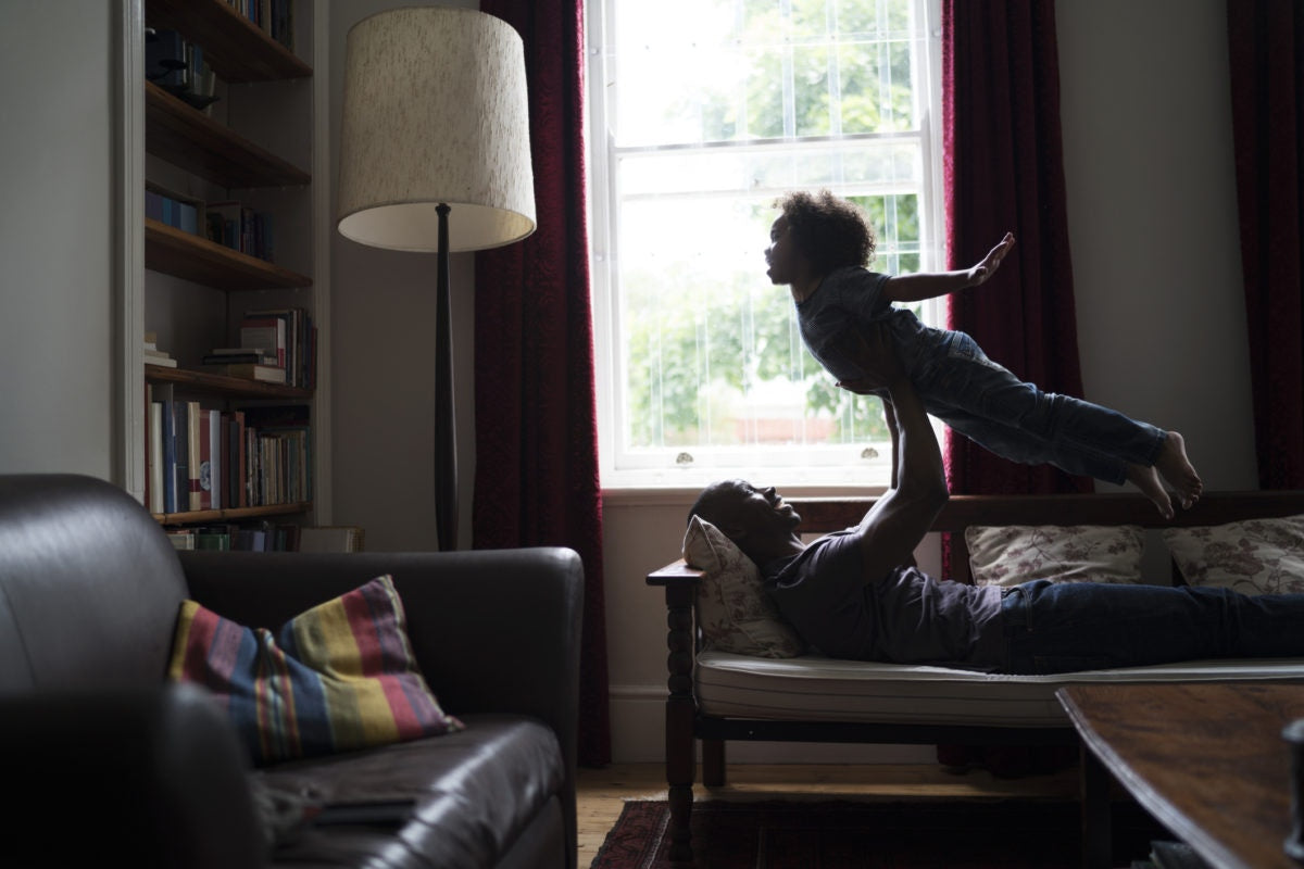 Father holding her child up above with his hands, lying on a couch